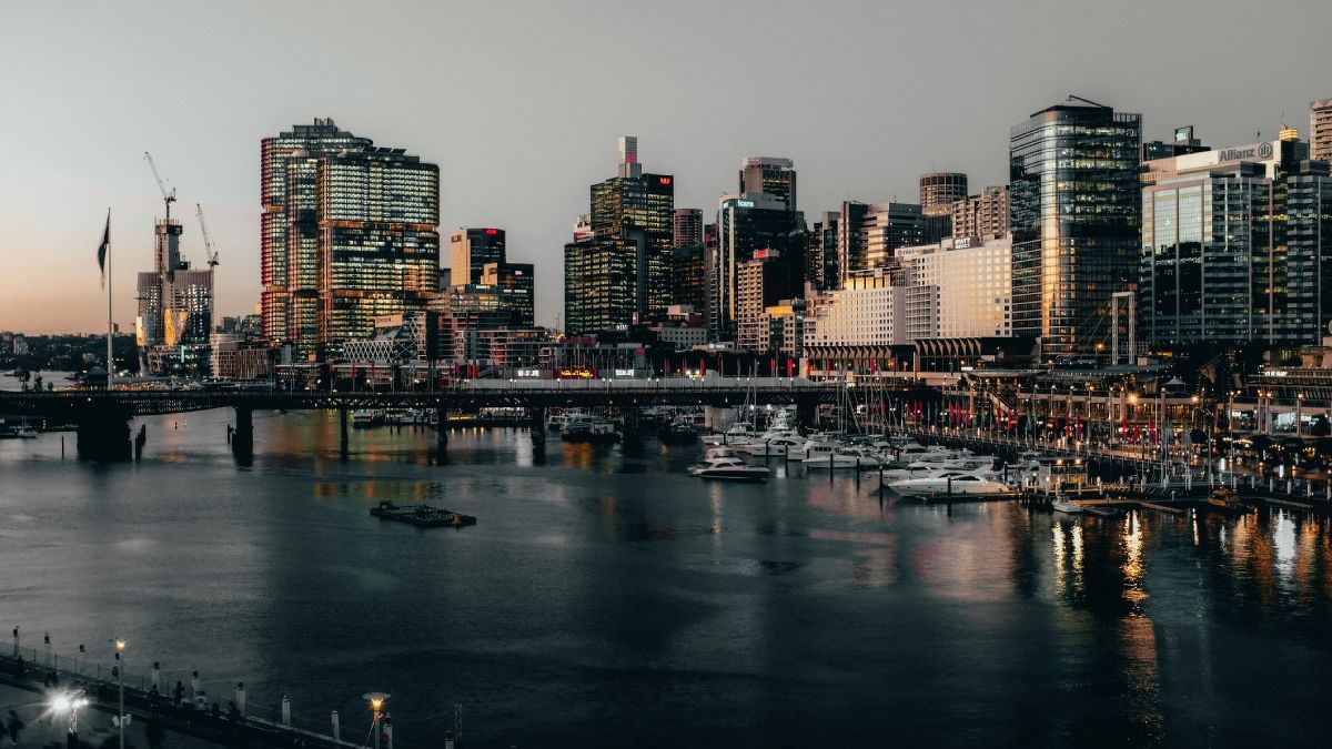 Skyline of Sydney, Australia, at dusk, showing commercial buildings, a bridge, and boats.